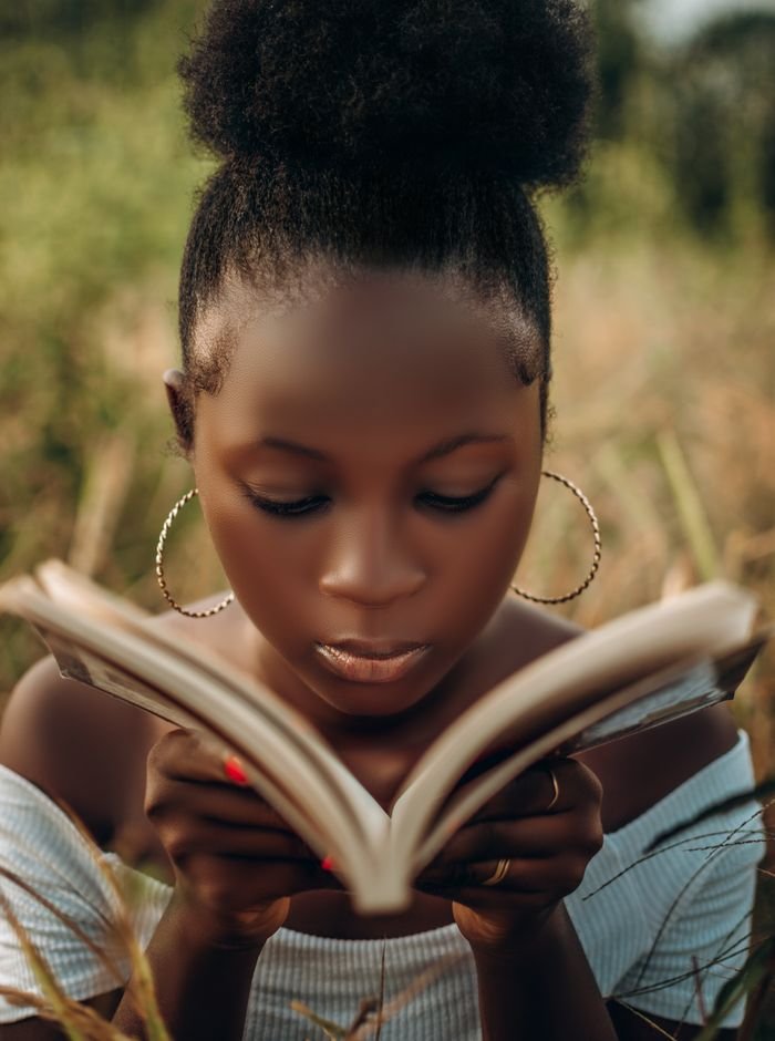 Close-up of a woman with hoop earrings reading a book outdoors in Keffi, Nigeria.