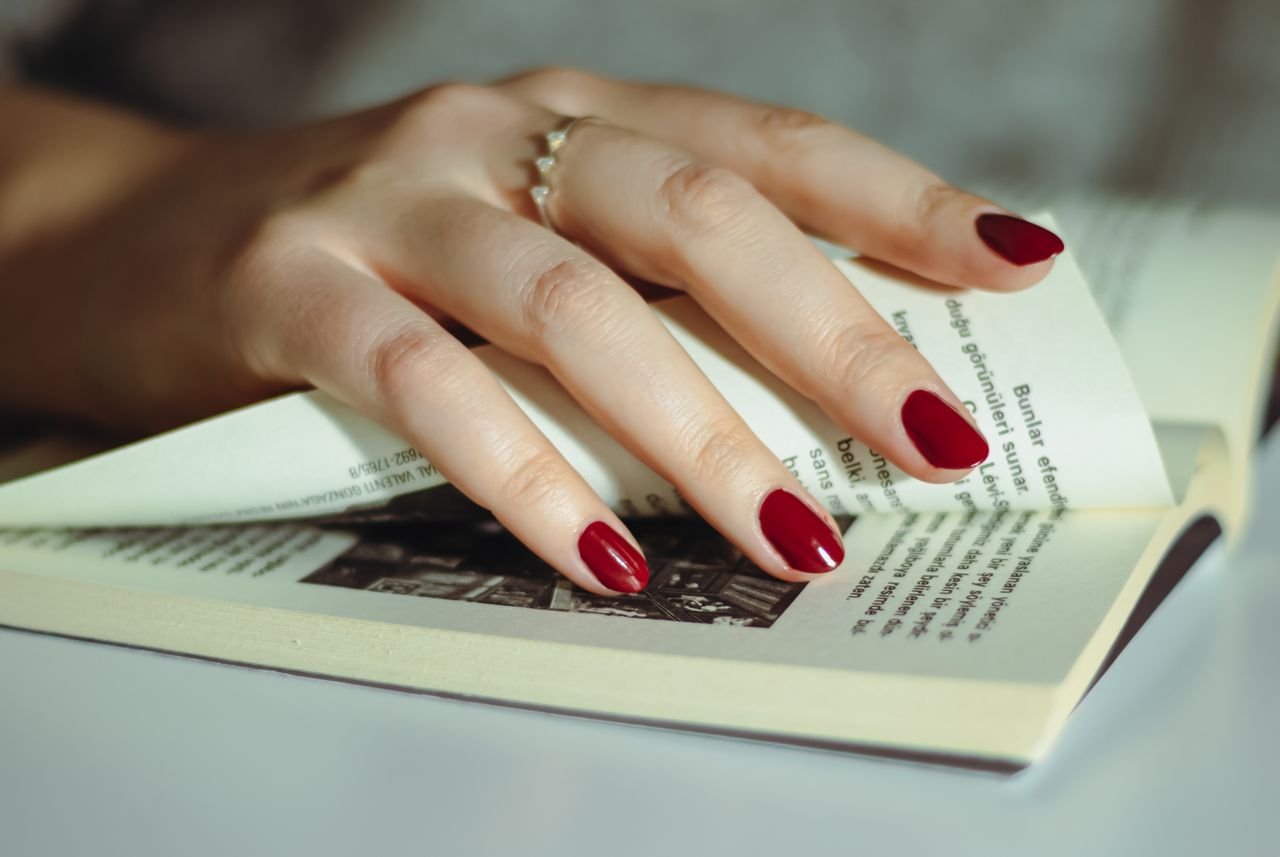 services-01 A hand with red nail polish flipping through book pages, symbolizing reading and literature.