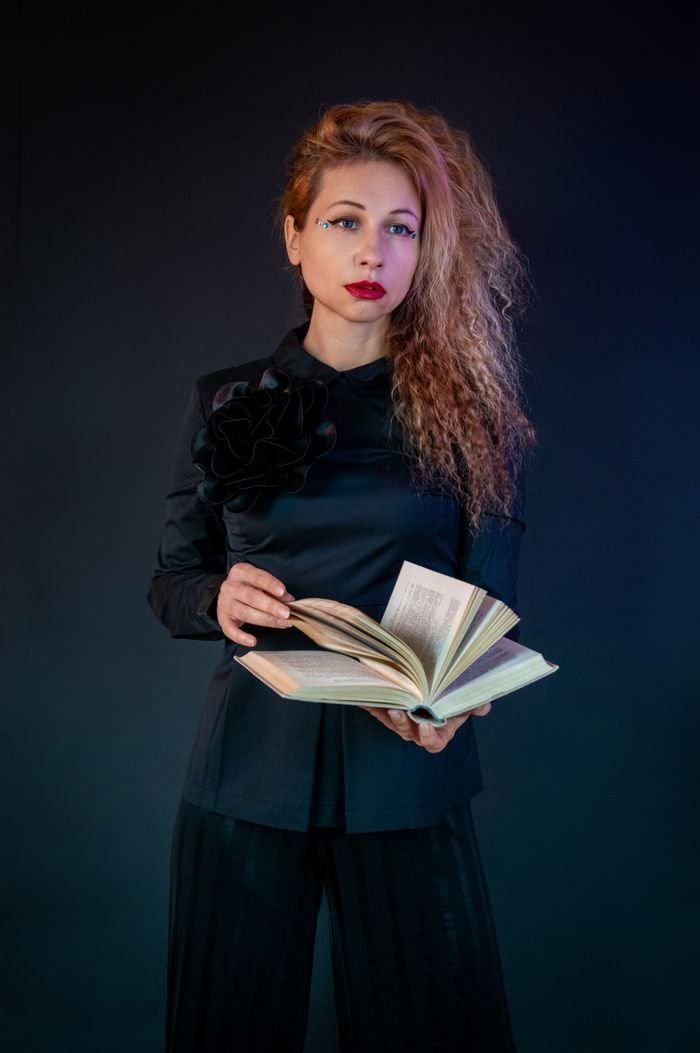 services-03 Stylish woman holding a book, captured against a dark studio background, exuding elegance and mystery.