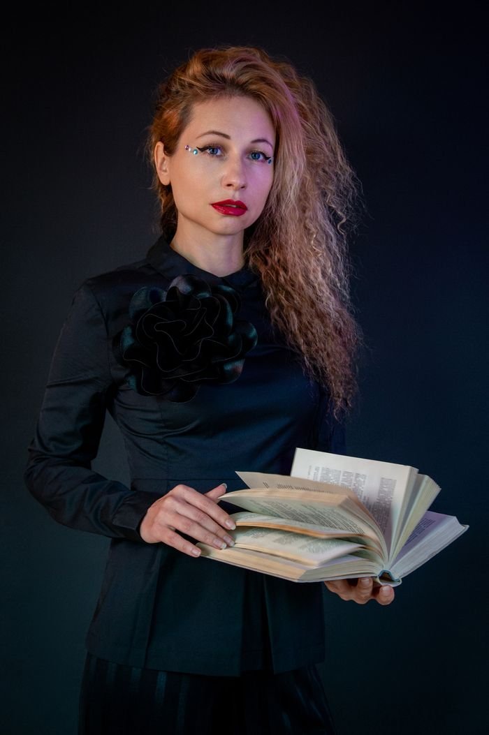 Stylish woman in black holding an open book, showing a thoughtful expression.