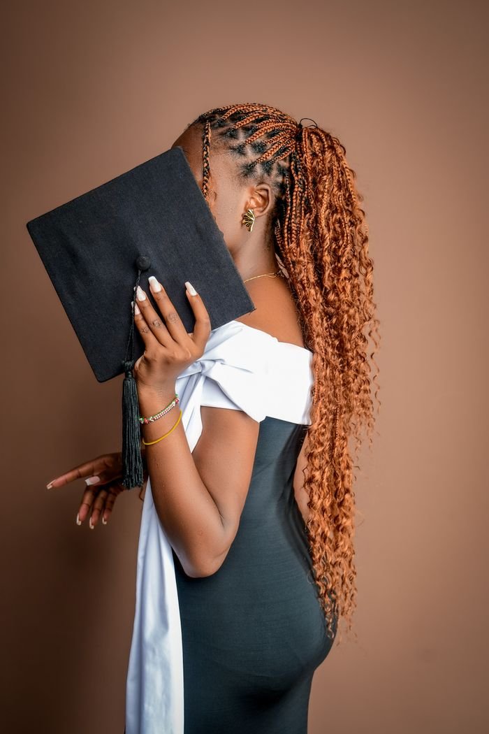 Woman in graduation attire holding cap, celebrating academic achievement.