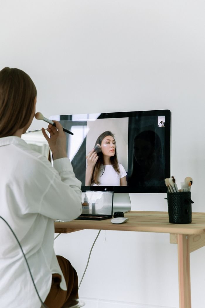 services-img Woman using makeup brush while following an online tutorial on skincare and beauty.