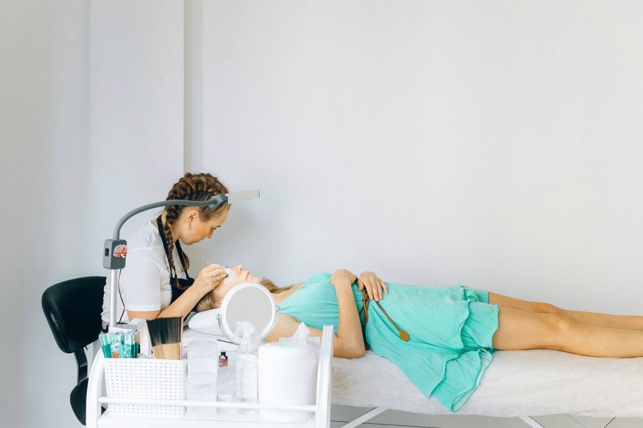 A beautician performing an eyebrow treatment on a client in a modern salon setting.