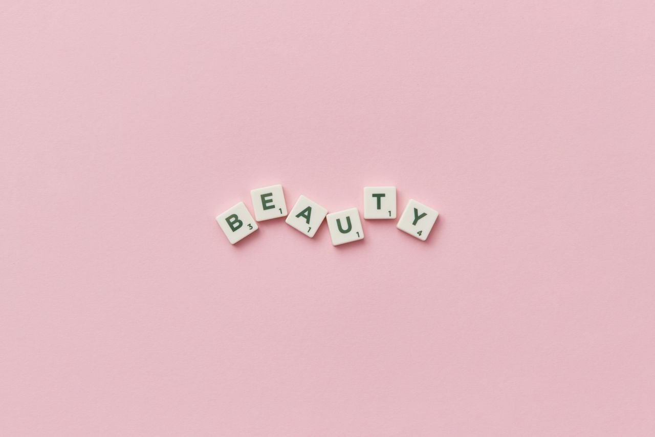 Scrabble tiles forming the word 'Beauty' on a soft pink background, top view, minimalist style.
