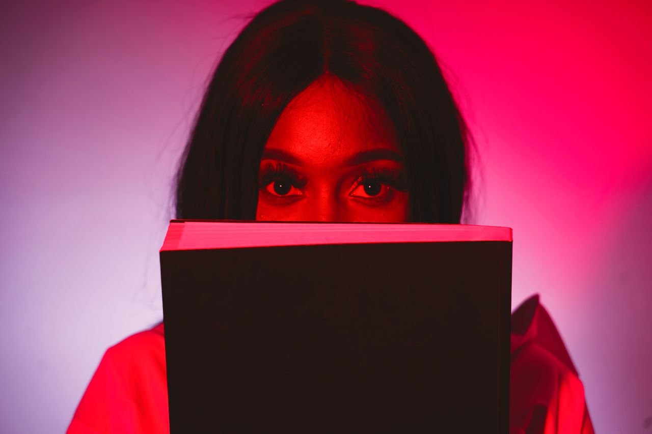 Close-up of a woman holding a book, bathed in red light, creating a mysterious and dramatic atmosphere.