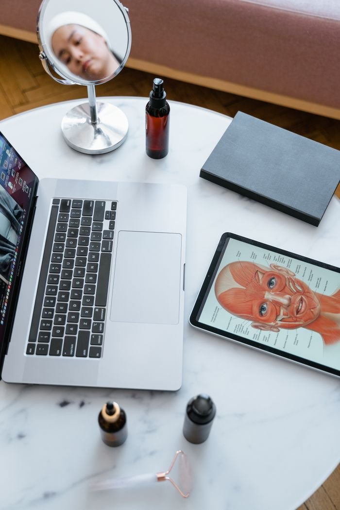 An overhead view of a tabletop with a laptop, tablet displaying human anatomy, and beauty products.