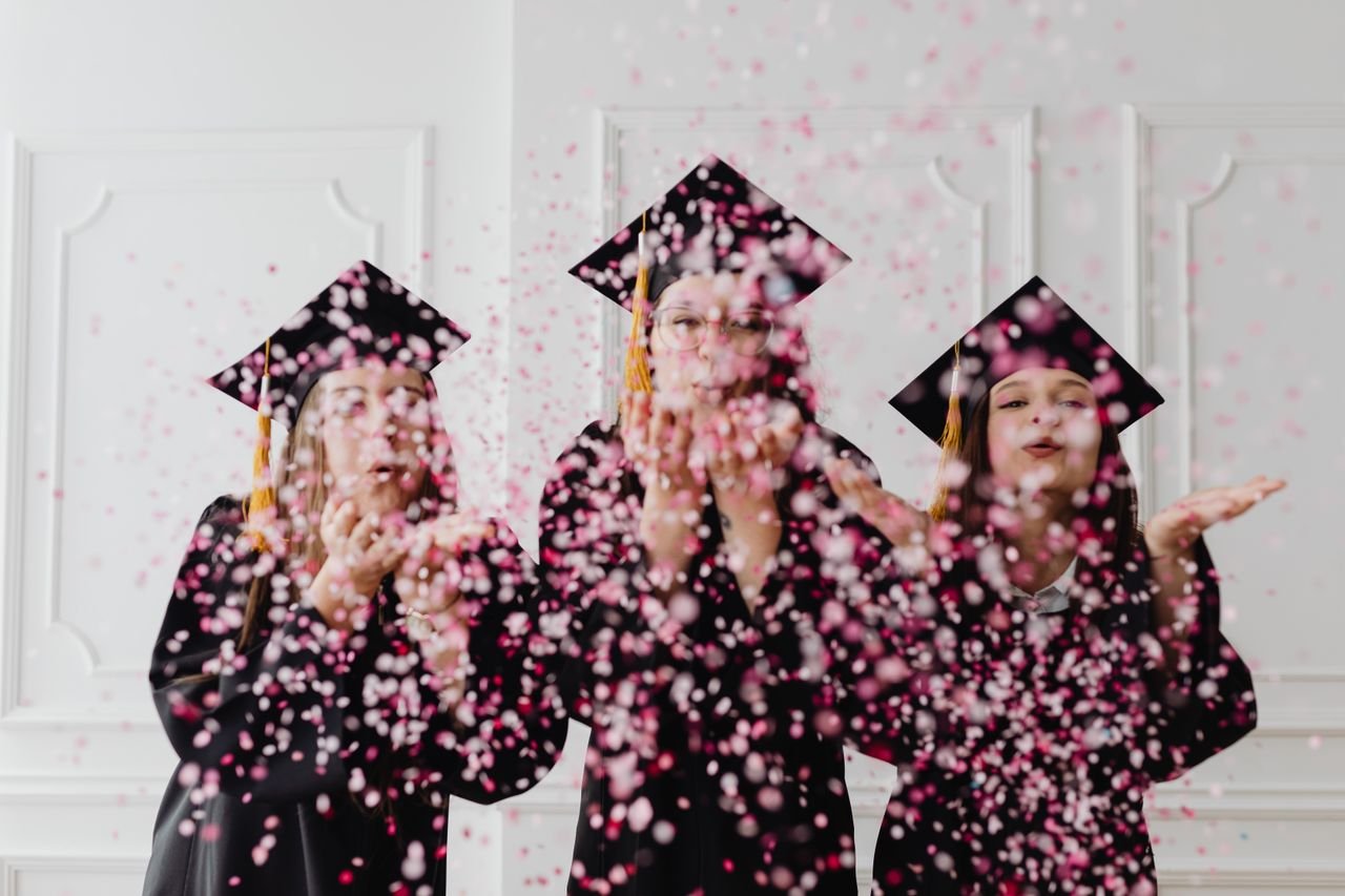 Three graduates celebrating with confetti indoor, expressing joy and achievement.